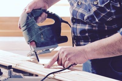 Midsection of man using power tool on wood at home