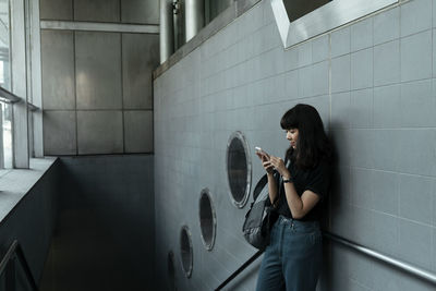 Side view of young woman playing guitar against wall