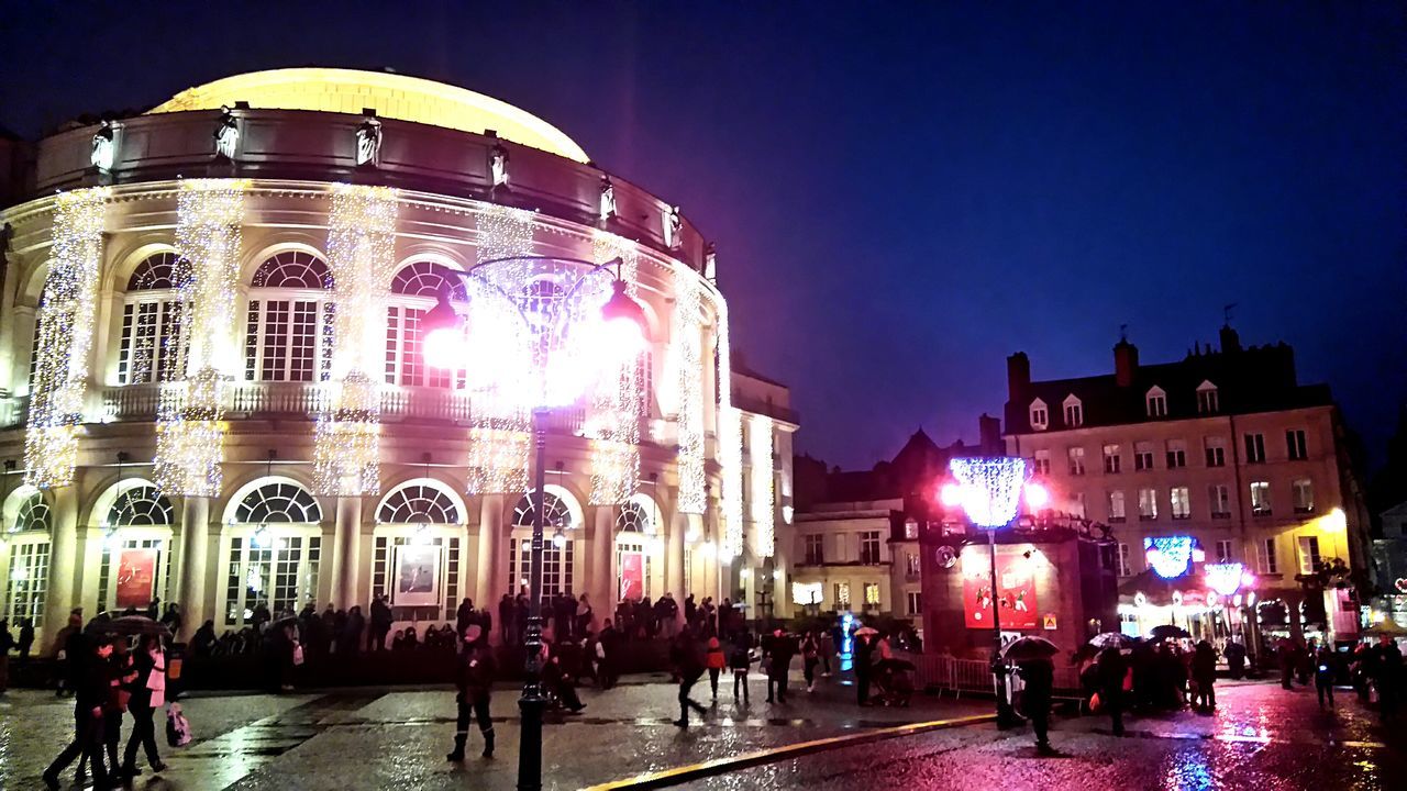 PEOPLE WALKING ON ILLUMINATED STREET AT NIGHT