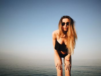 Portrait of beautiful woman wearing sunglasses at beach against clear blue sky