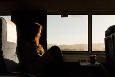 Side view of woman sitting by window in train during sunset