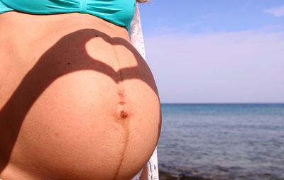 Midsection of woman by sea against sky