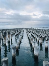 Wooden posts in sea against sky