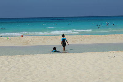 Siblings at beach against sky