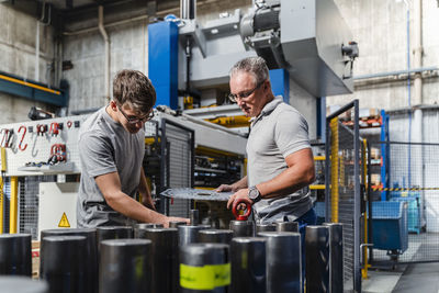 Male engineer examining product with mature technician in illuminated industry