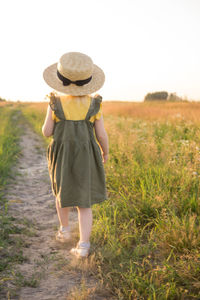 A little blonde girl in a straw hat walks in a field with a bouquet of daisies. 