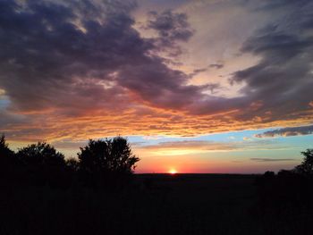Silhouette trees on landscape against dramatic sky during sunset