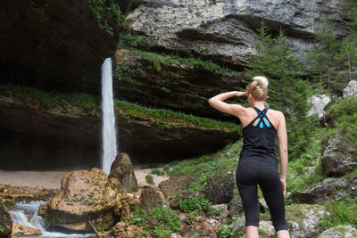 Rear view of woman standing on rock by waterfall