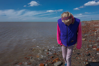 Girl walking at beach against blue sky during sunny day