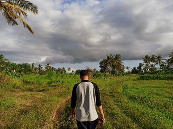 Rear view of man standing on field against sky