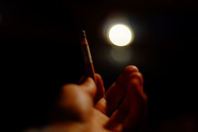 Cropped hand smoking against illuminated light in darkroom