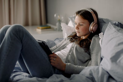 Teenage girl in bed watching movie through digital tablet at home