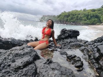 Full length of young woman standing on rock against sea