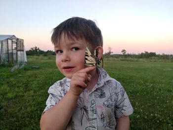 Portrait of cute boy holding butterfly on field against sky