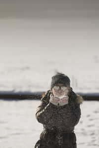 Portrait of woman blowing snow on field during winter