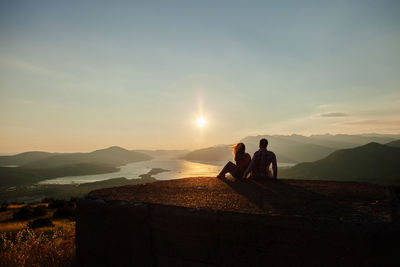 Couple on built structure against sky during sunset