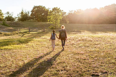 Rear view of woman and daughter hiking on grass at park during sunset