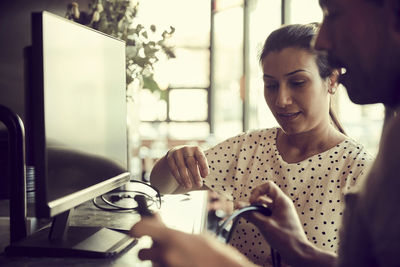 Male and female owners adjusting cable of computer monitor in cafe