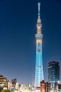 Communications tower in city against clear blue sky at night