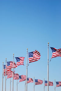 Low angle view of national flags against clear blue sky