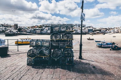 Stacked crab nets at harbor against cloudy sky