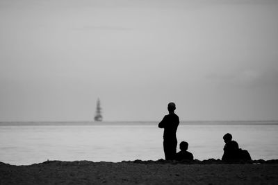 Silhouette people on beach with boat in distance