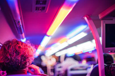 Rear view of woman sitting in illuminated bus