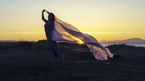 Woman standing on beach against sky during sunset