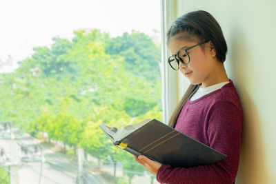Girl reading book by window at home