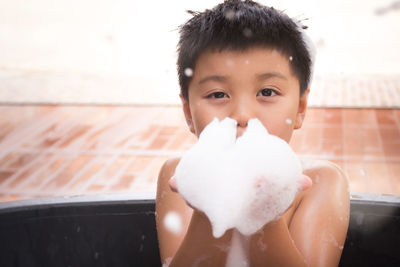 Close-up portrait of boy playing with soap sud in bathtub