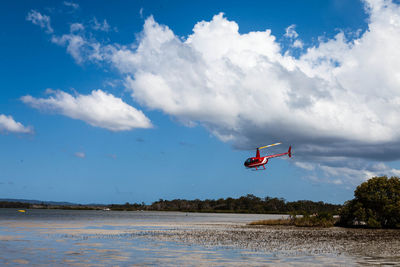 Helicopter flying over lake against cloudy sky