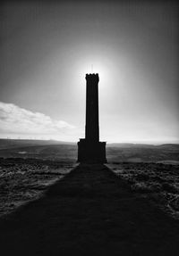 Lighthouse on field by building against sky