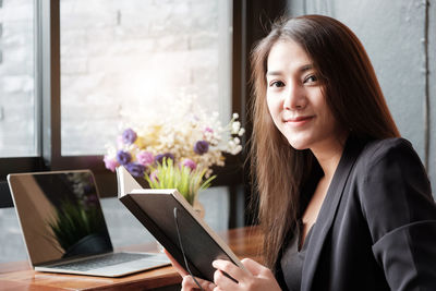 Portrait of beautiful woman holding book by laptop on table