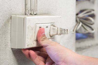 Close-up of person hand pressing push button on electrical outlet