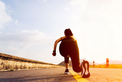 Rear view of woman exercising on road against sky