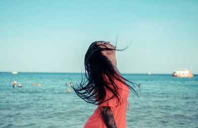 Rear view of woman standing at beach against clear sky