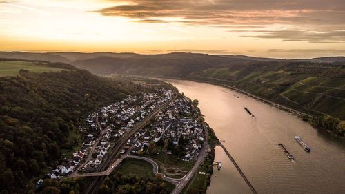 Aerial view of river amidst cityscape and landscape against sky during sunset