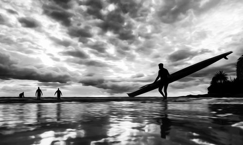 Silhouette people at seaside against cloudy sky