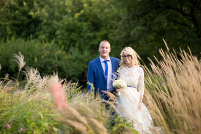 Portrait of newlywed couple standing by grass at park