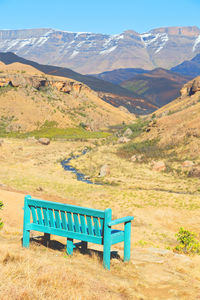 Empty bench on field against mountain range