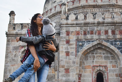 Low angle view of woman carrying boy while standing against building