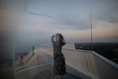 Woman standing by railing against sky during sunset