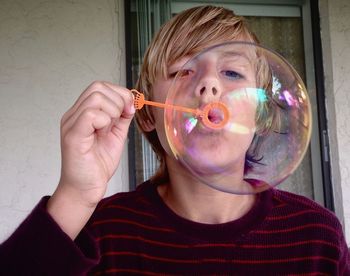 Close-up of teenage boy blowing bubble against wall