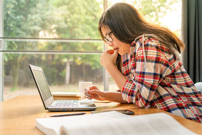 Midsection of woman using phone while sitting on table