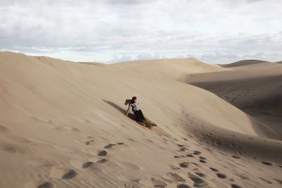 Man riding motorcycle on sand dune in desert against sky