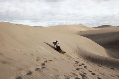 Man on sand dune at desert against sky