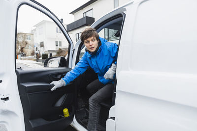 Young delivery woman looking away while disembarking from van