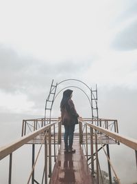 Rear view of woman standing on pier against sky