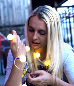 Close-up of young woman holding illuminated string lights