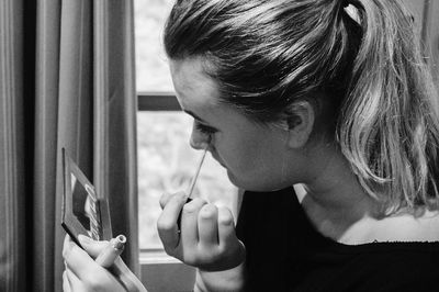 Woman looking into mirror while applying eyeliner